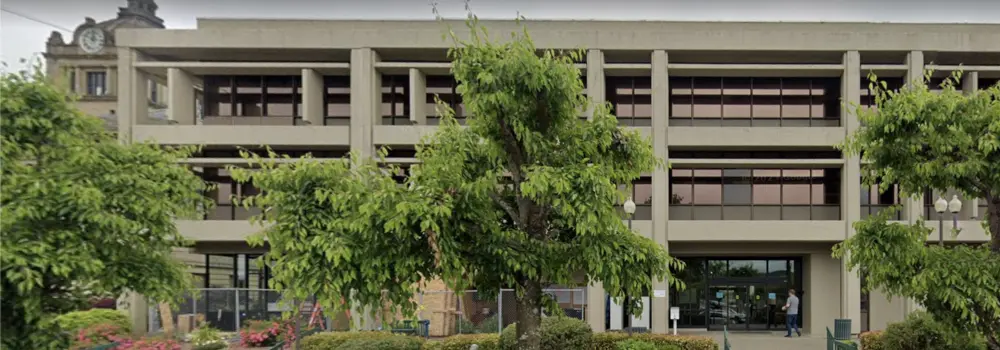 Civic office building entrance framed by trees and landscaping.