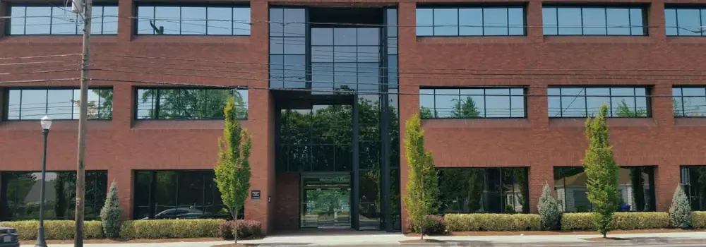 Front entrance of a red-brick office building with large windows and landscaped grounds.