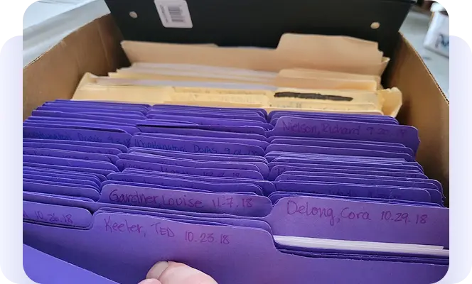 Box of labeled purple and manila paper file folders.