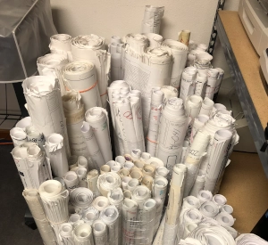 Rolled white technical drawings or paper plans stored in bins.
