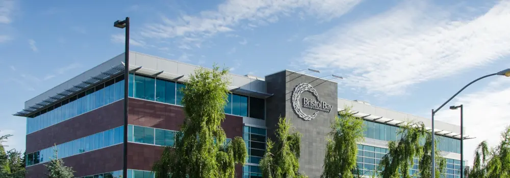 Bristol Bay office building with glass windows and trees in front.