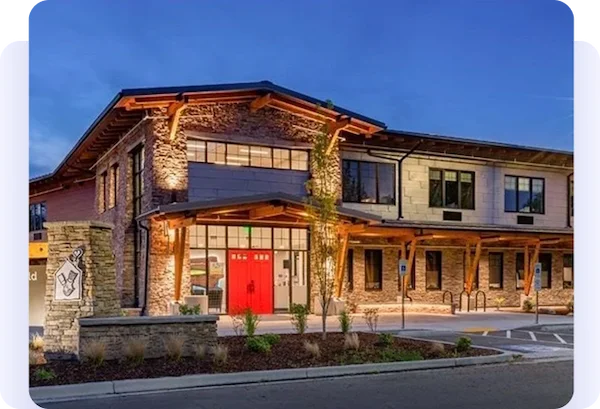 Modern two-story building with stone accents and bright red entrance doors at dusk.