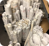 Rolled white technical drawings or paper plans stored in bins.